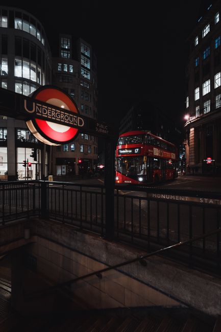 Night view of a London street with double-decker bus and Underground sign, capturing urban life.