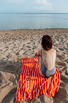 Young woman sitting on the sandy beach during summer vacation, enjoying the ocean view.