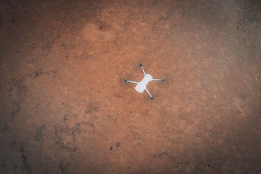 White drone captured from above on a reddish-brown wet ground. Abstract aerial view.