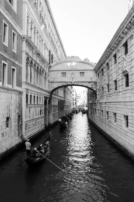 Black and white image of gondolas navigating a Venetian canal beneath the Bridge of Sighs.