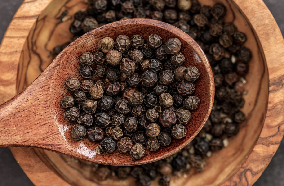 Dried black peppercorns on a wooden spoon