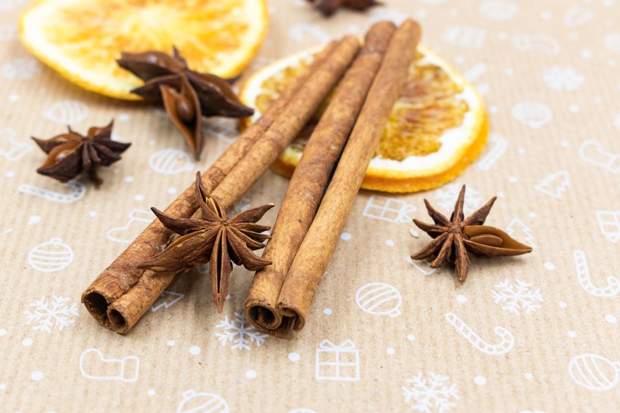 Close-up of cinnamon sticks, star anise, and dried orange slices on festive paper.