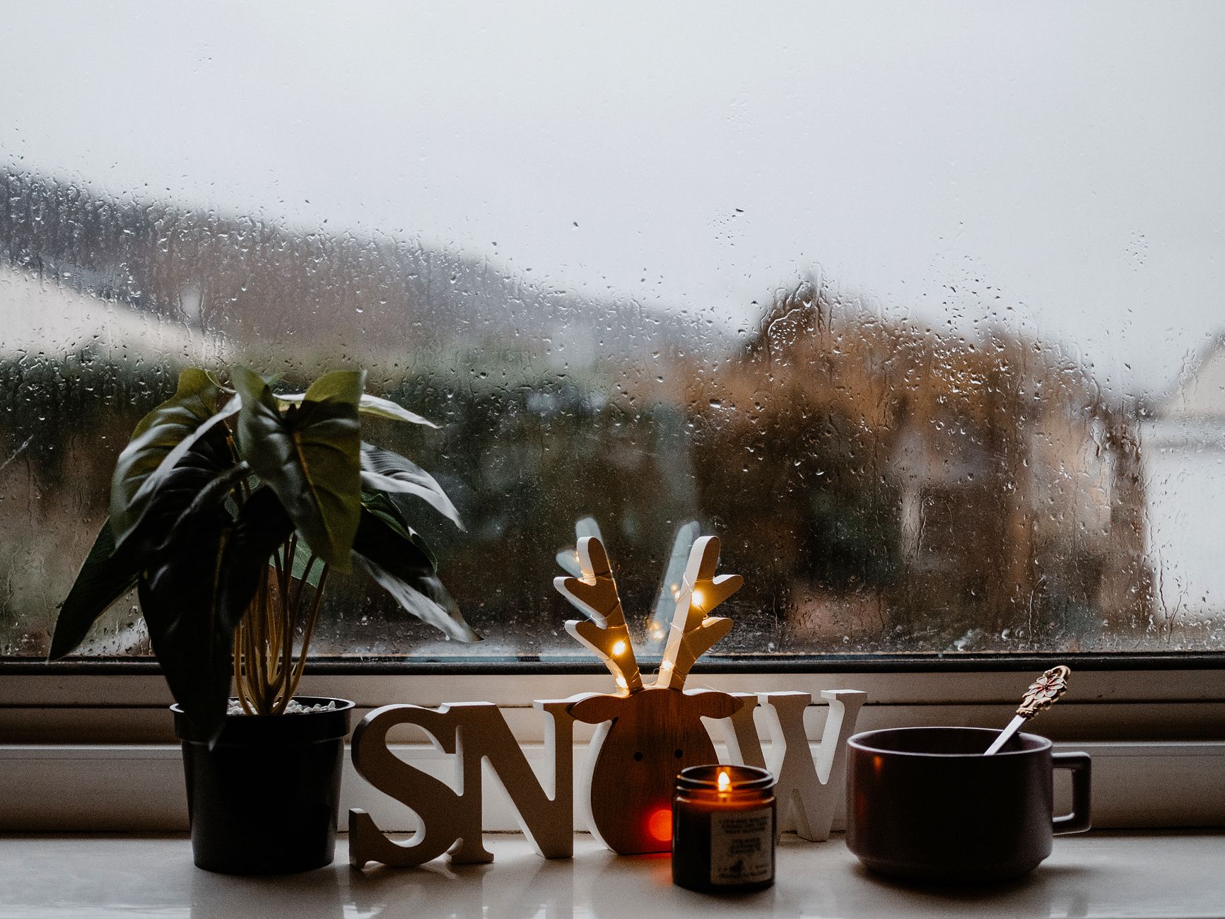 Warm and cozy winter scene with a candle, potted plant, and rainy window for a festive atmosphere.