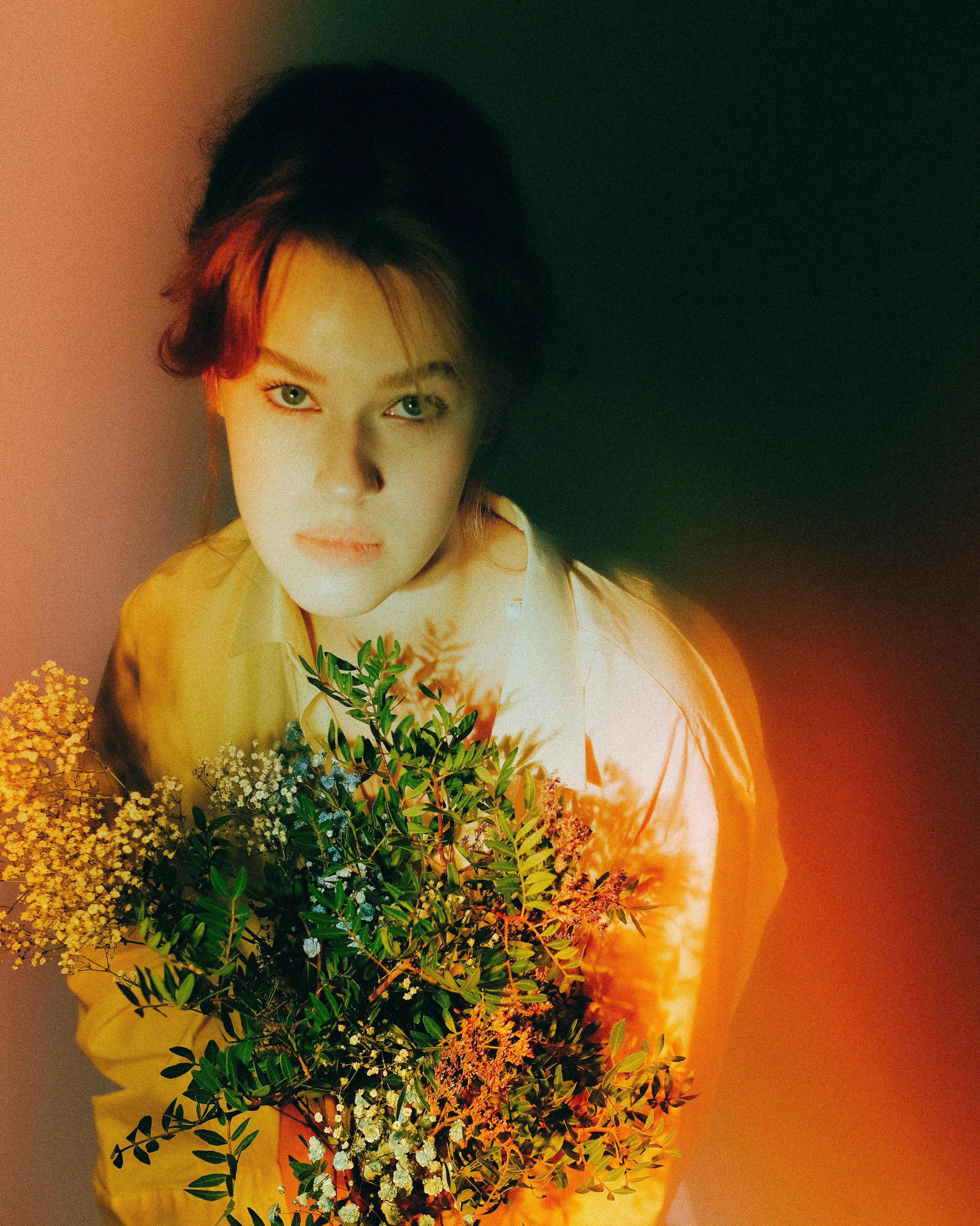 Dramatic portrait of a young red-haired woman holding flowers, embracing vibrant warmth and contrast.