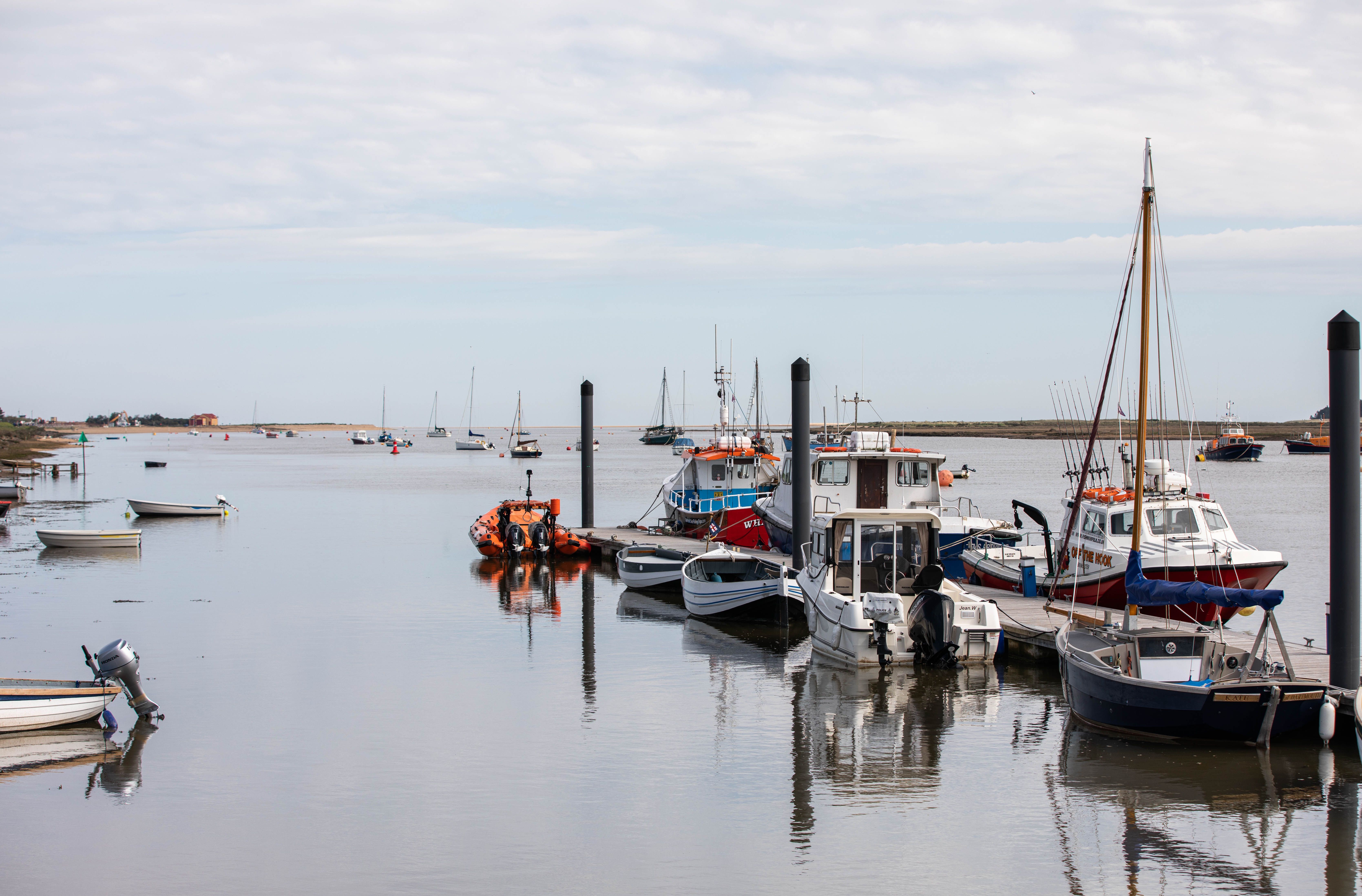 Tranquil scene of boats docked along a boardwalk under a cloudy sky in England, reflecting on calm waters.
