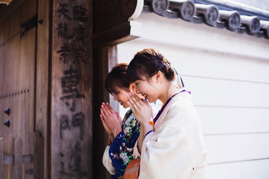 2人の着物を着た女性が京都の寺院の門で祈り、日本の伝統を受け入れています。