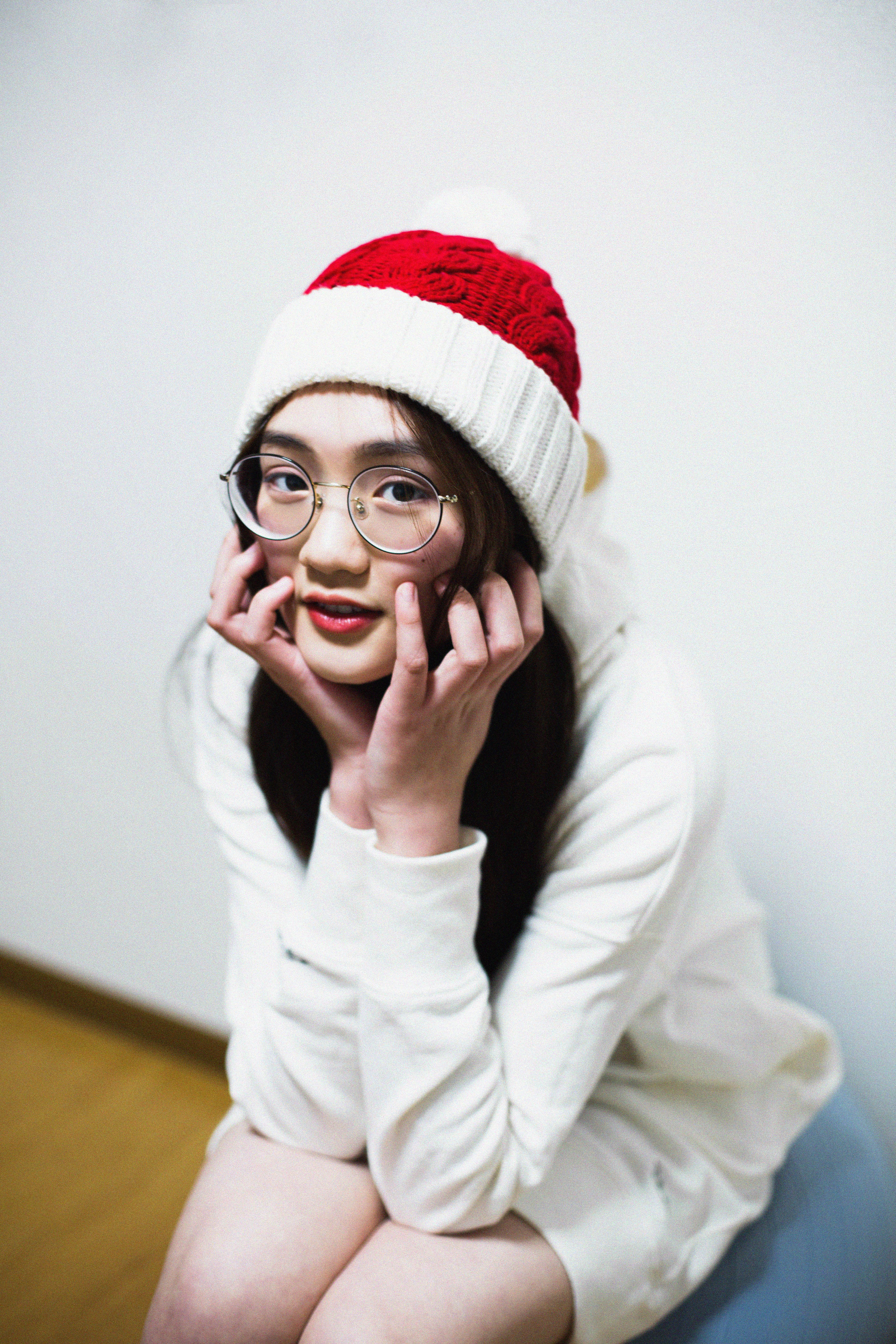 Young woman in Santa hat and eyeglasses smiling indoors, festive mood.