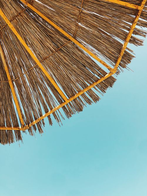 Free Low angle shot of a straw beach umbrella under a vibrant blue sky, ideal for summer themes. Stock Photo