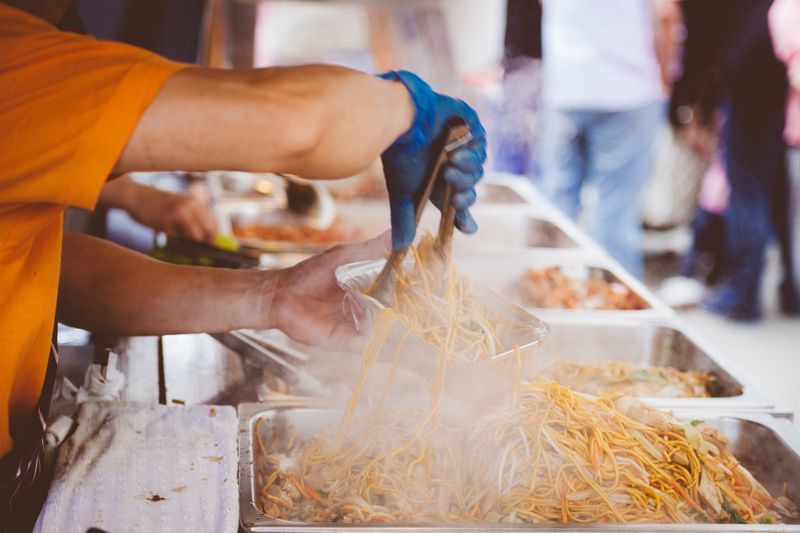 A street vendor serving freshly cooked noodles at a bustling outdoor market.
