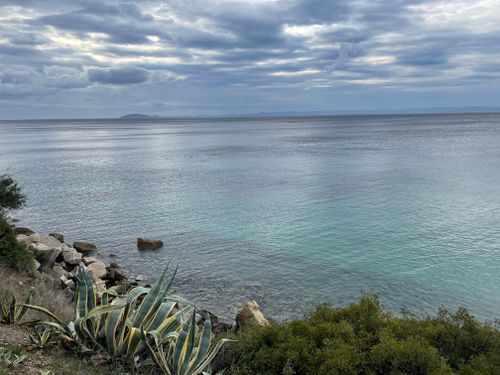 Free Beautiful coastal view of Greece with calm sea and lush plants under a cloudy sky. Stock Photo