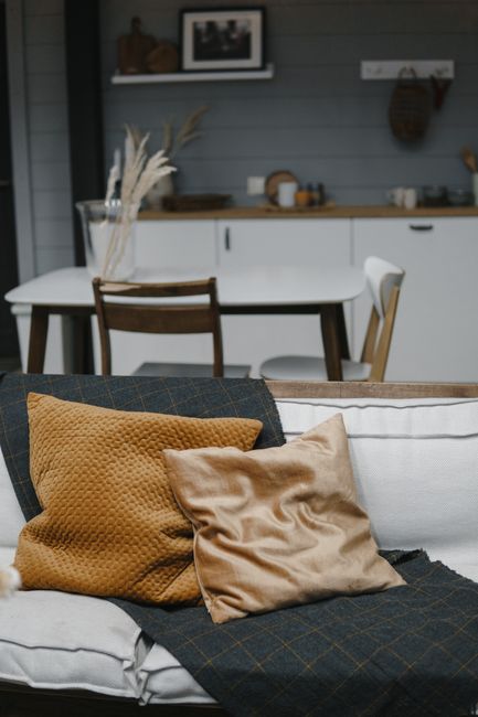 Stylish living space featuring mustard and beige pillows on a sofa with a modern dining area in the background.