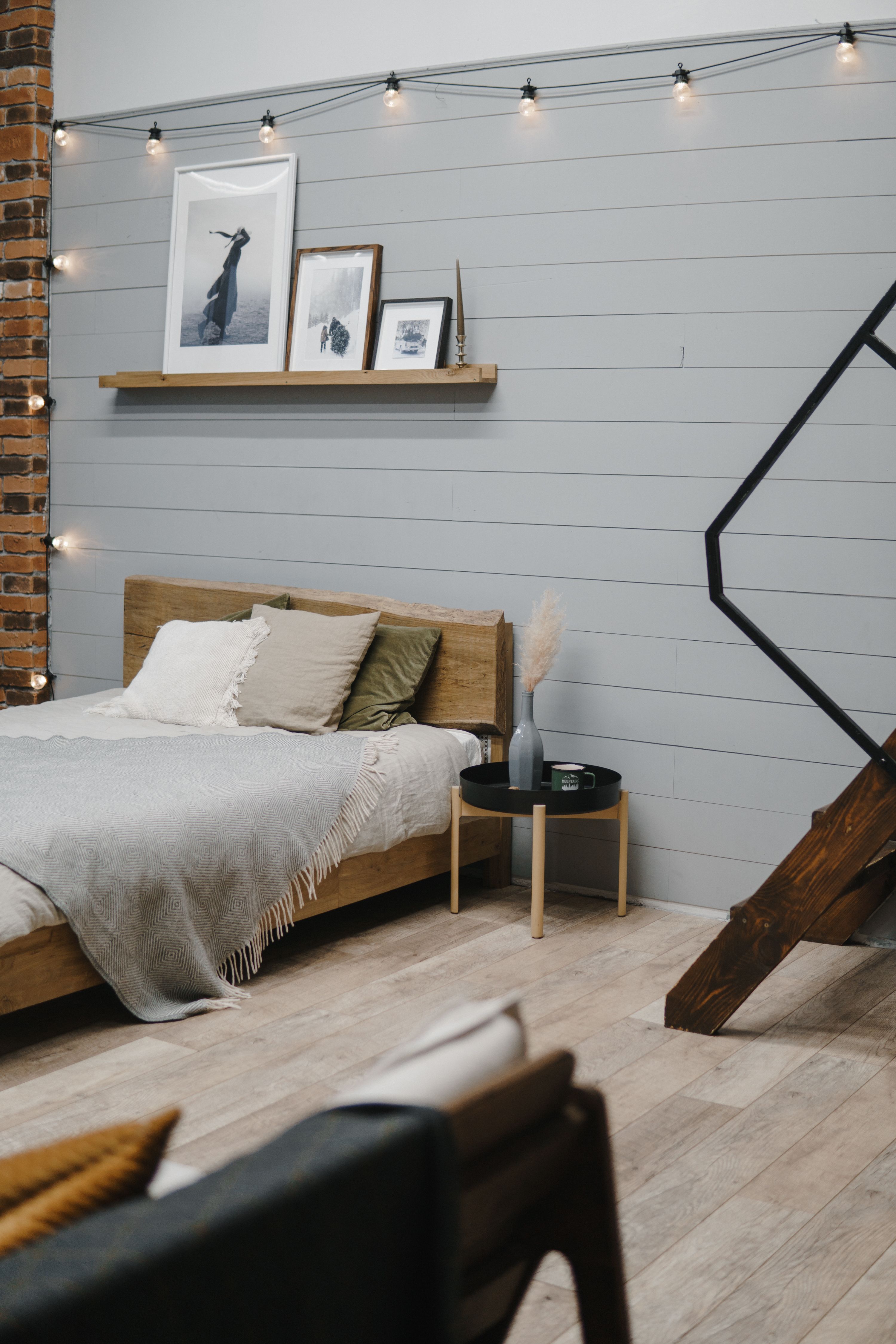 Bedroom wall with floating picture ledge shelf and string lights above the bed