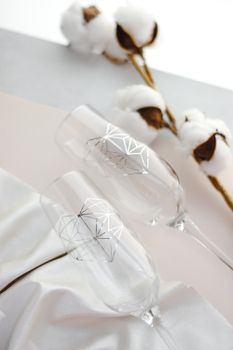 Artistic still life featuring elegant champagne glasses with geometric patterns and cotton stems.
