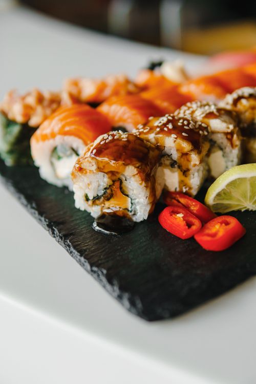 Free Appetizing sushi rolls with salmon, sesame seeds, and a hint of spicy red chili on a slate platter. Stock Photo