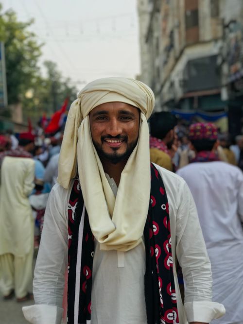 Free A joyful man wearing a traditional turban and scarf, amidst a vibrant street festival, exuding cultural charm. Stock Photo