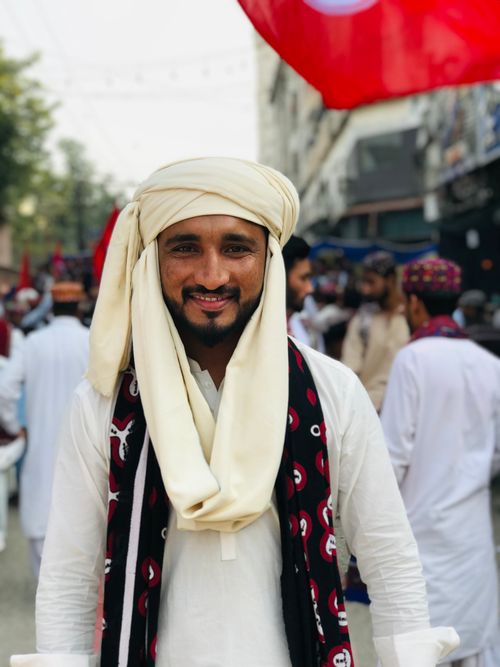 Free Bearded Asian man in traditional clothing smiling at outdoor cultural event. Stock Photo
