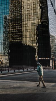 A person in a blue jacket walks by a reflective skyscraper, capturing urban life.