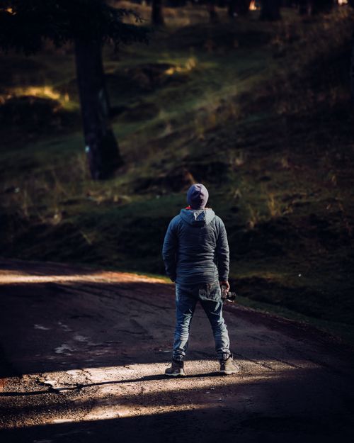 Free Person in a hoodie holding a camera, standing on a forest pathway. Outdoors scene. Stock Photo