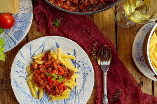 Free Delicious penne pasta topped with savory tomato sauce and herbs on a rustic table setting. Stock Photo