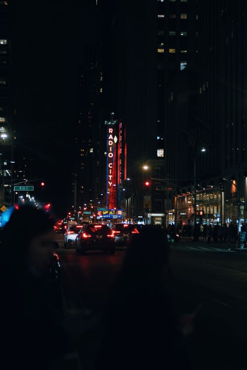 Free Busy night street scene in downtown NYC featuring cars and illuminated Radio City sign. Stock Photo