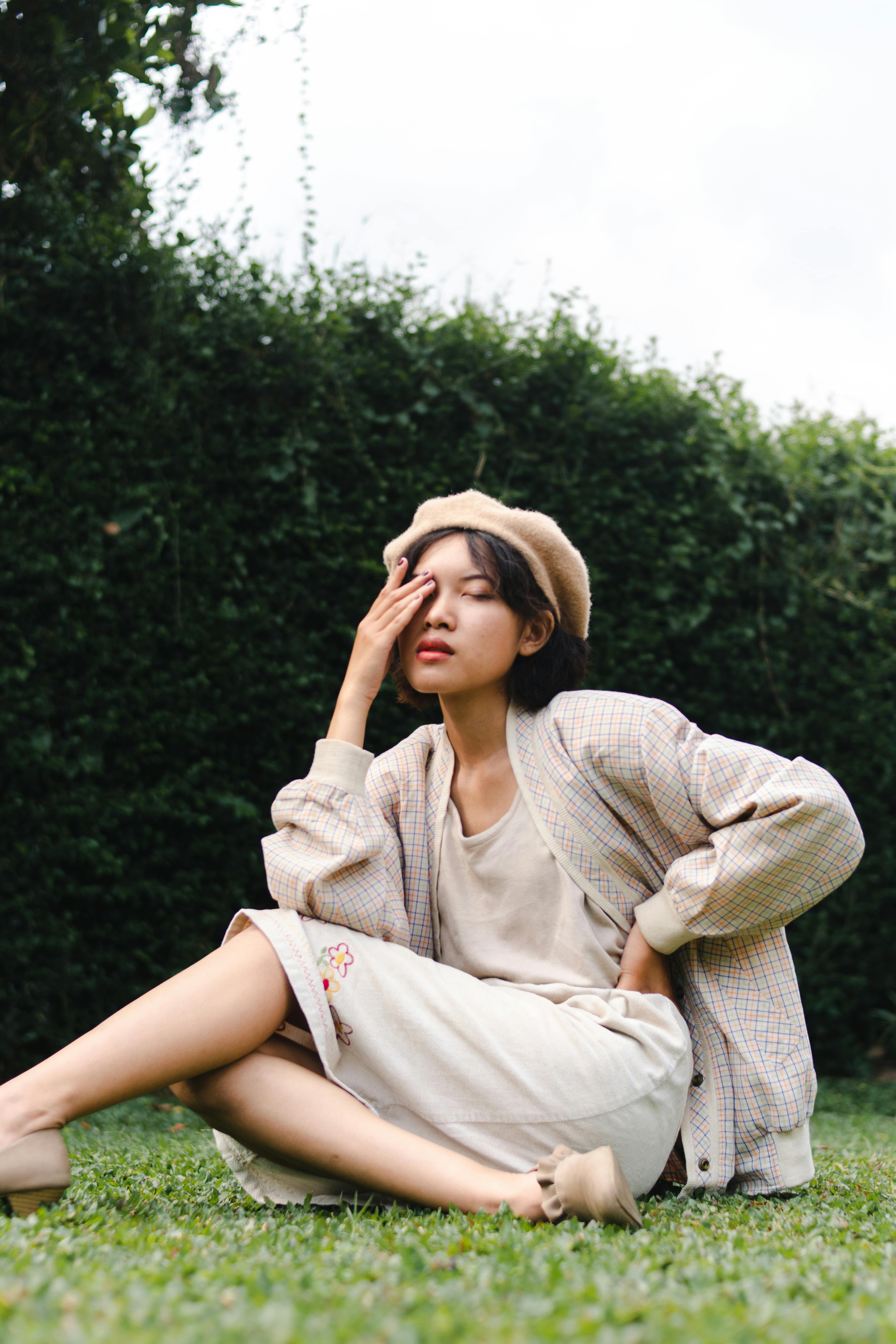 Fashionable woman in beret sitting outdoors posing thoughtfully, wearing a neutral outfit.