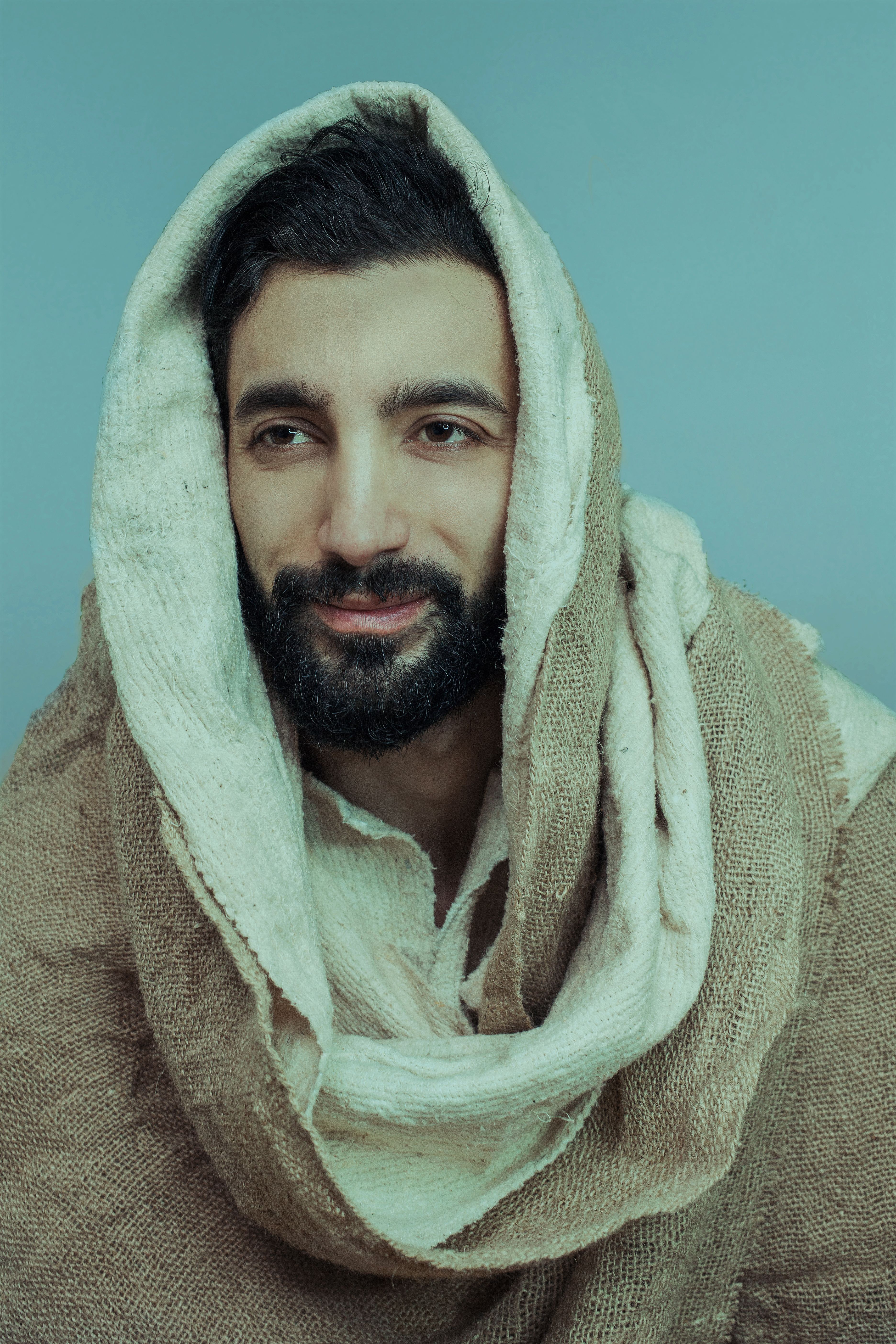 A captivating portrait of a man with a beard, wrapped in a headscarf against a blue background.