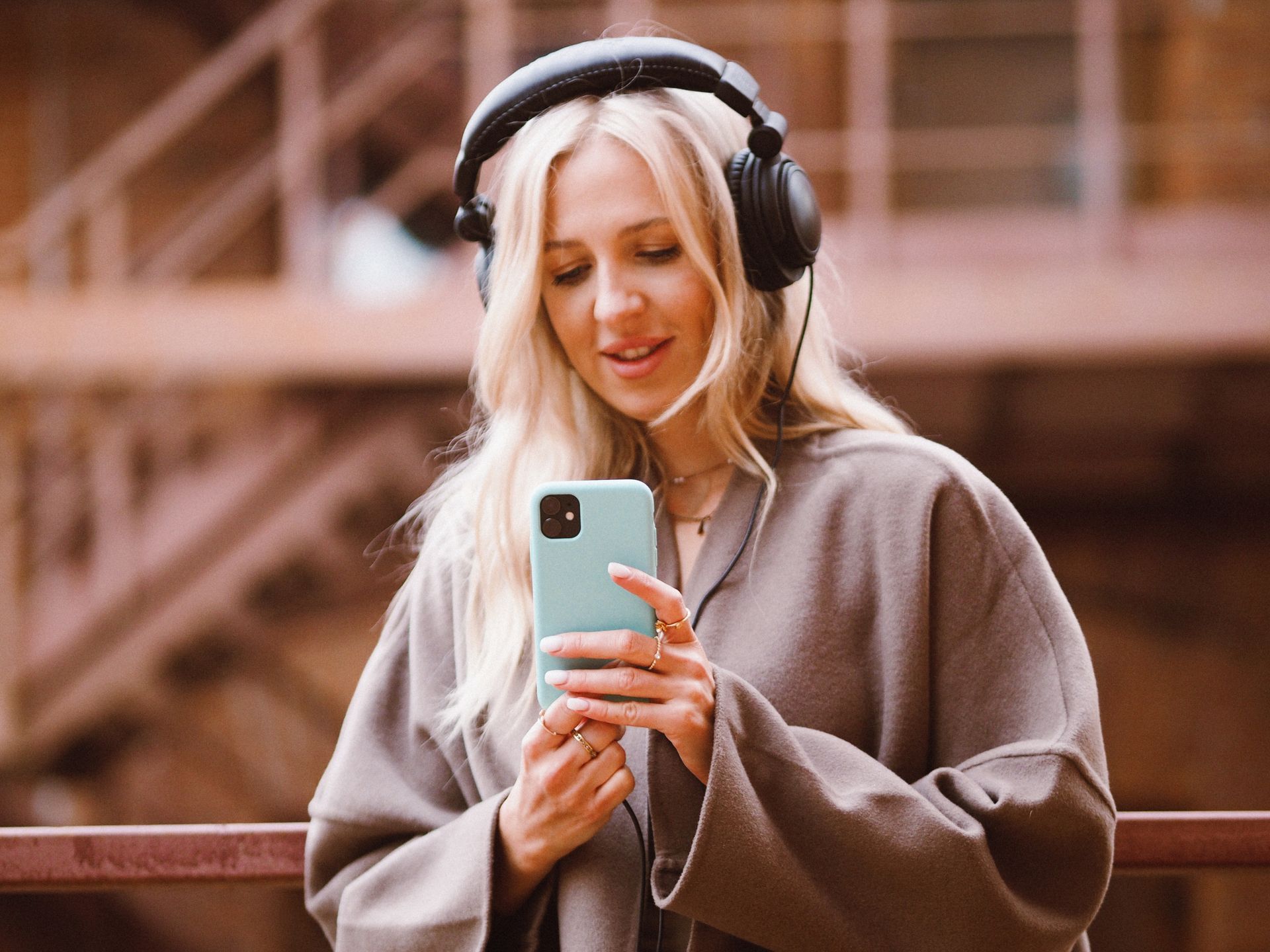 Blond woman enjoying music on headphones while using a smartphone outdoors in New York City.