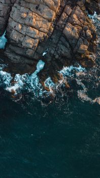 Aerial view capturing waves crashing against a rugged rocky cliff. Perfect for coastal themes.