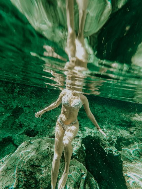 A woman in a bikini gracefully swimming underwater, showcasing fluid movements and reflections.