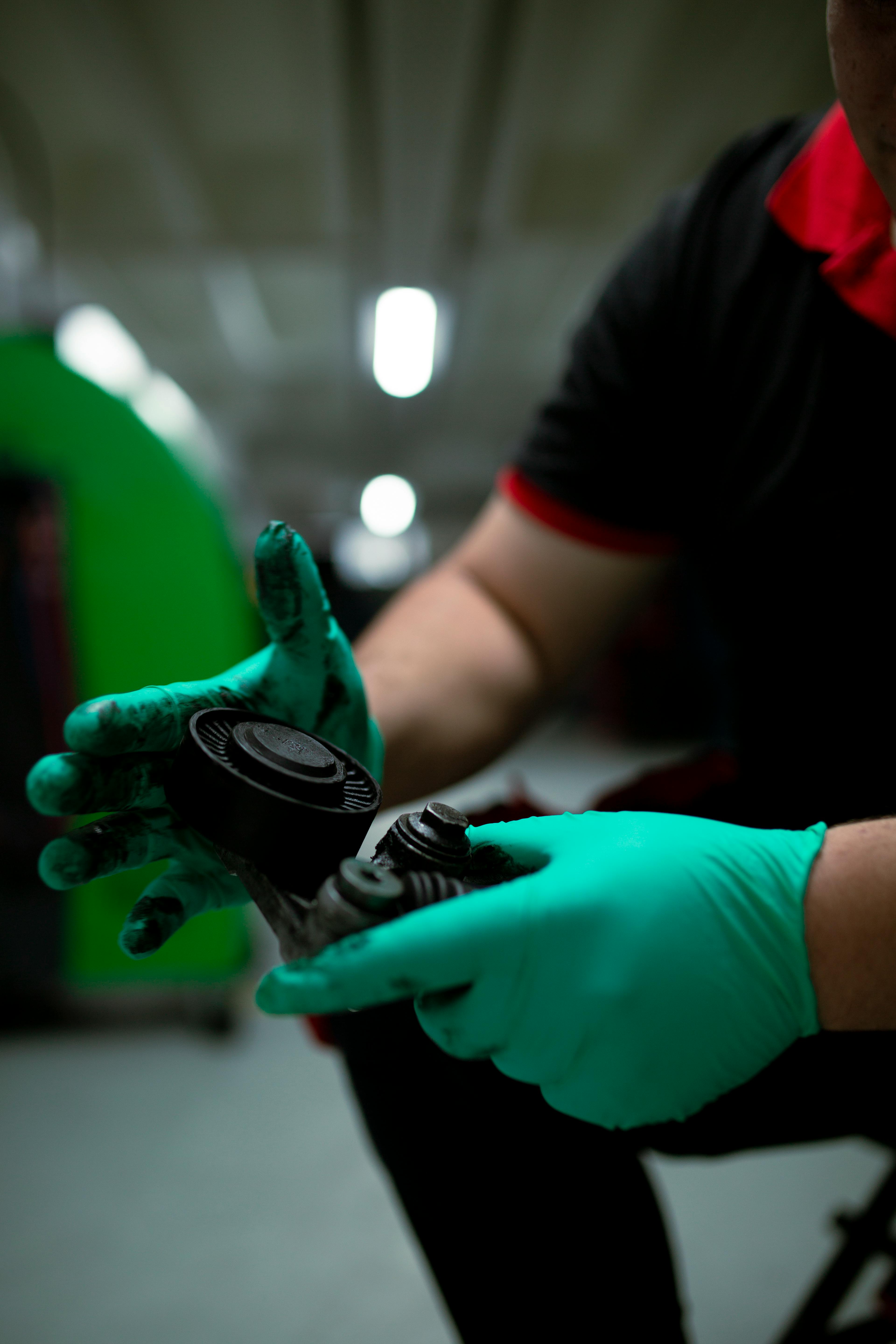 Close-up of a mechanic with gloves examining a car part in a workshop setting.