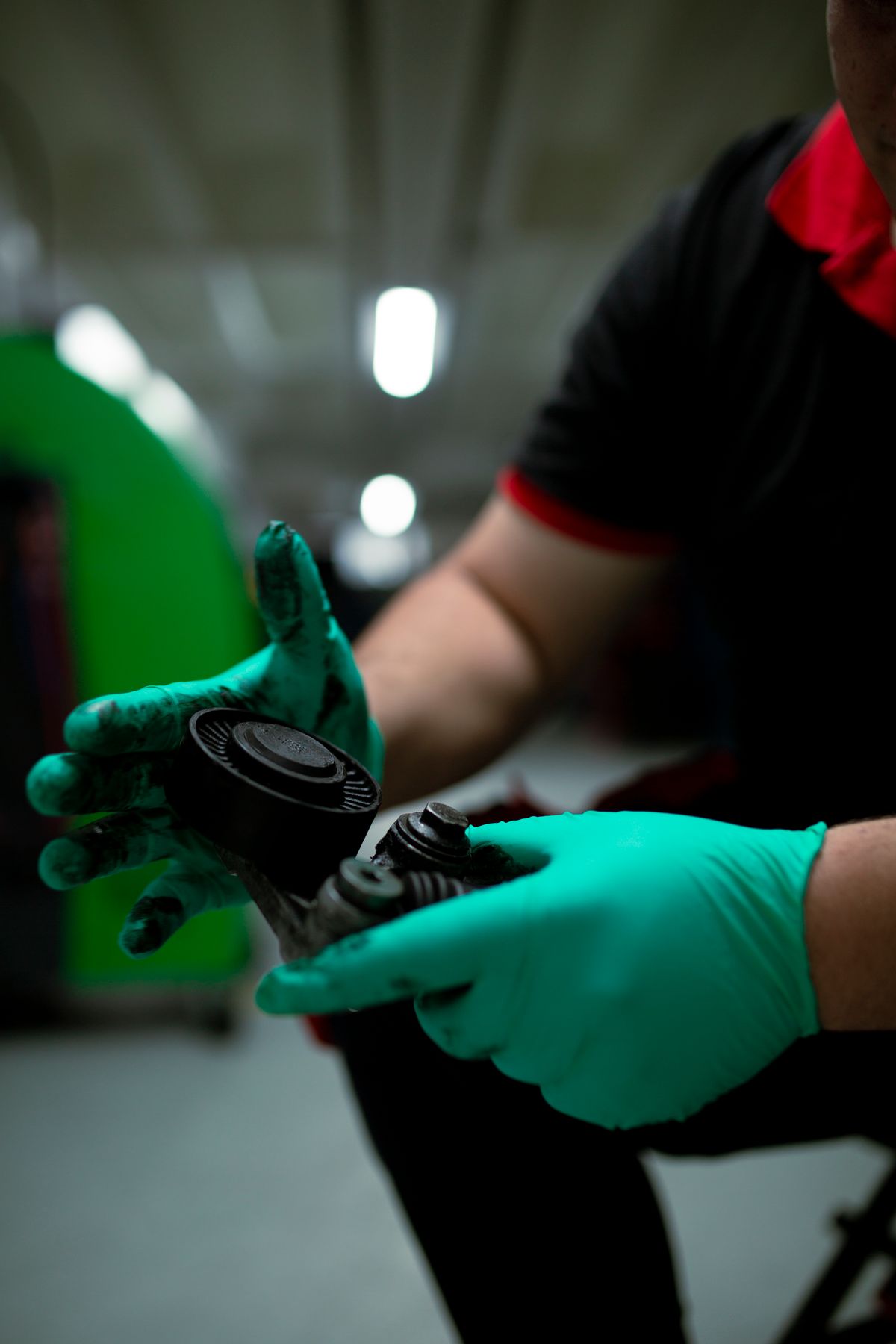 Gloved hands turning over a belt tensioner pulley to inspect it