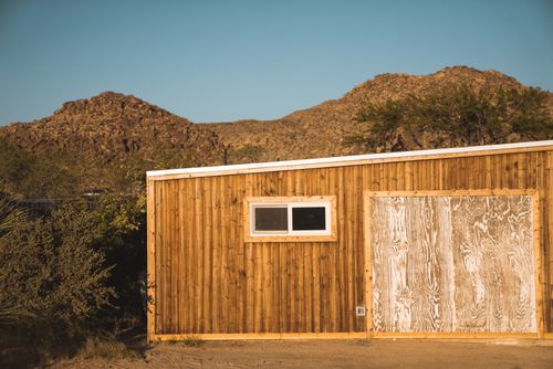 Free A wooden cabin stands against the rugged desert mountains of Joshua Tree, California, under a clear blue sky. Stock Photo