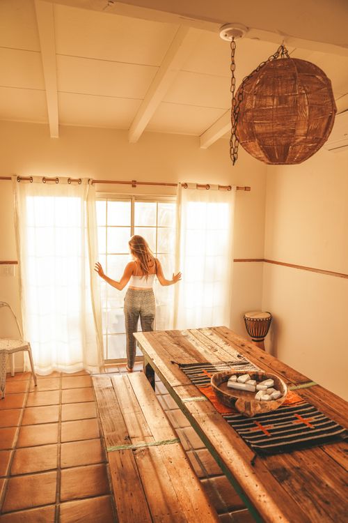 Free A woman admires sunlight through curtains in a Joshua Tree home, embracing tranquility. Stock Photo