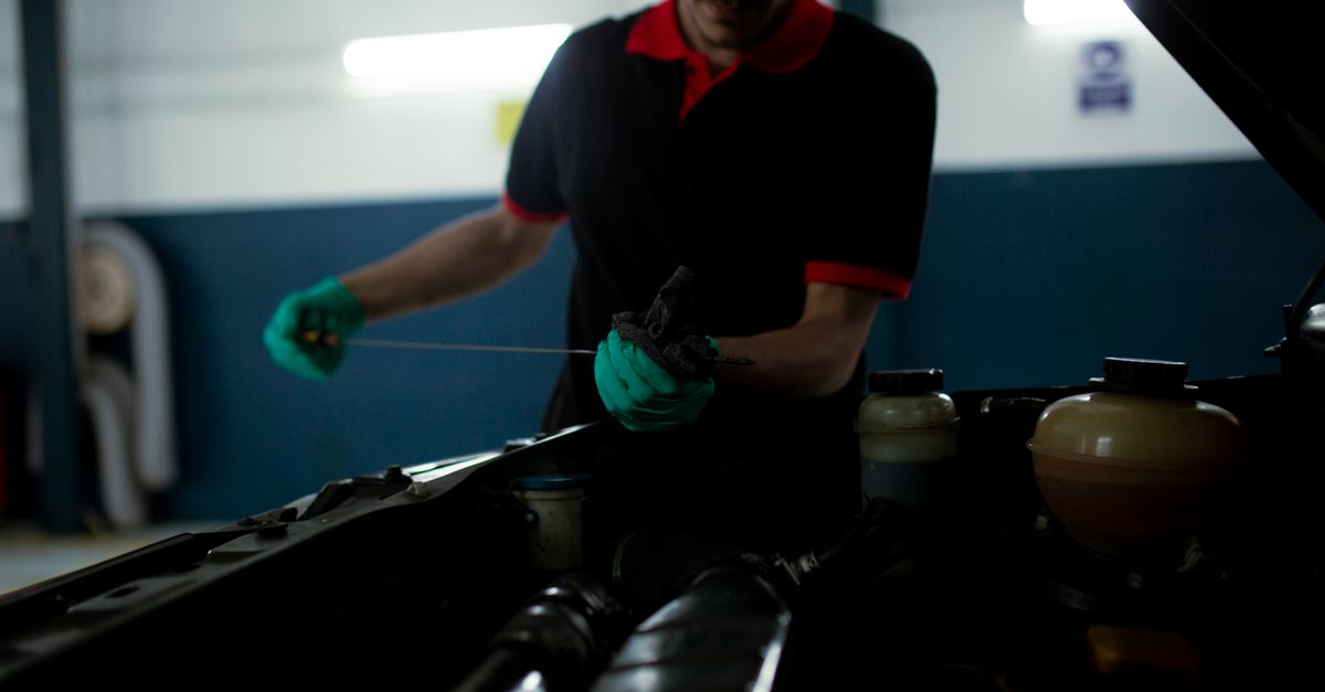 Mechanic examining a car engine's oil level using a dipstick in a garage setting.