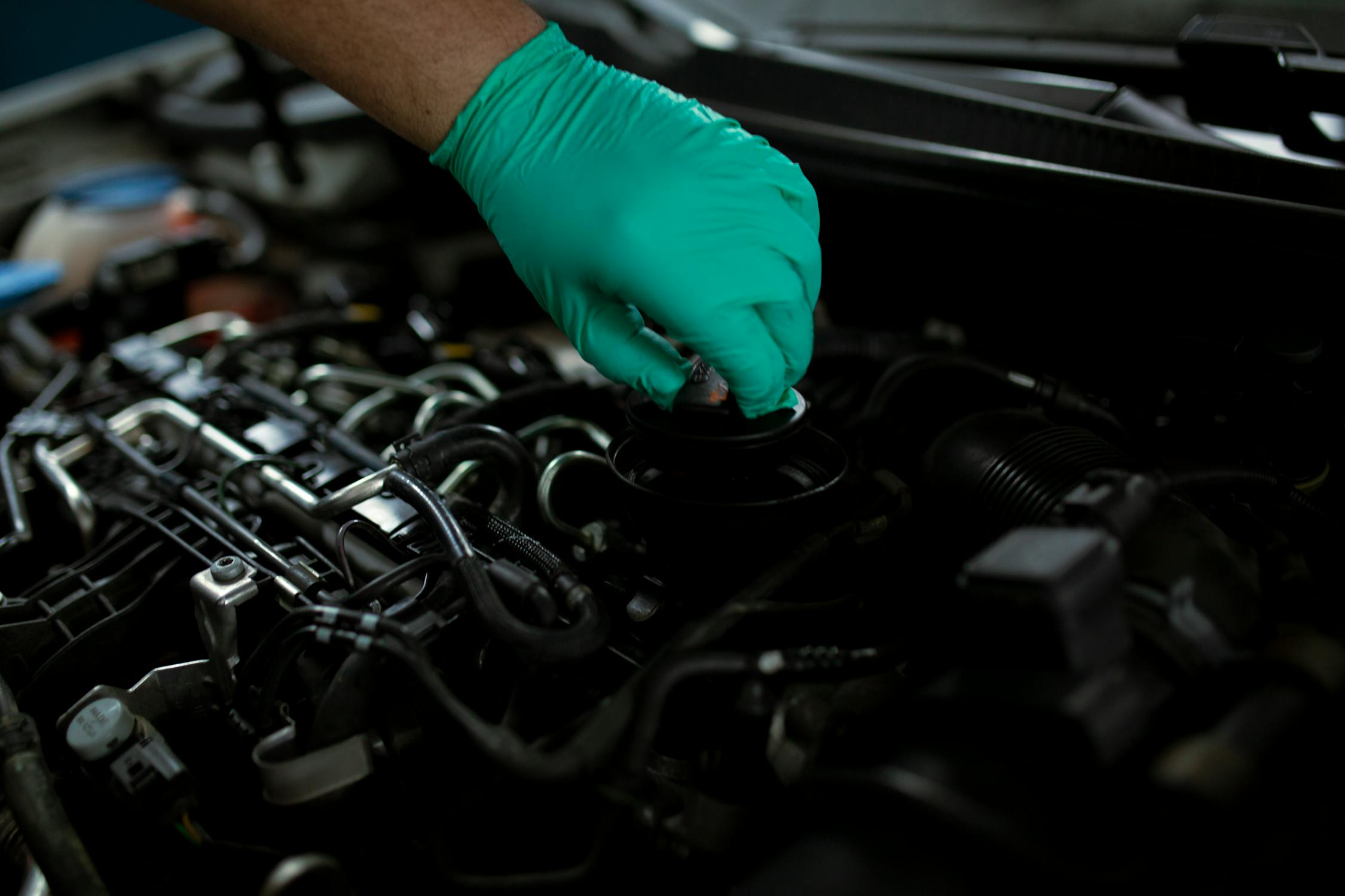 A Mechanic working on a car under the hood wearing teal gloves