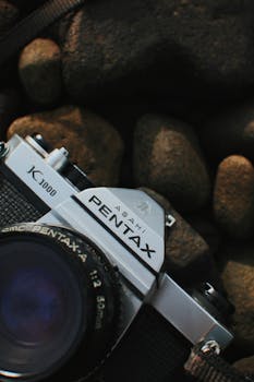 Detailed view of a classic Pentax K1000 camera resting on natural stones.
