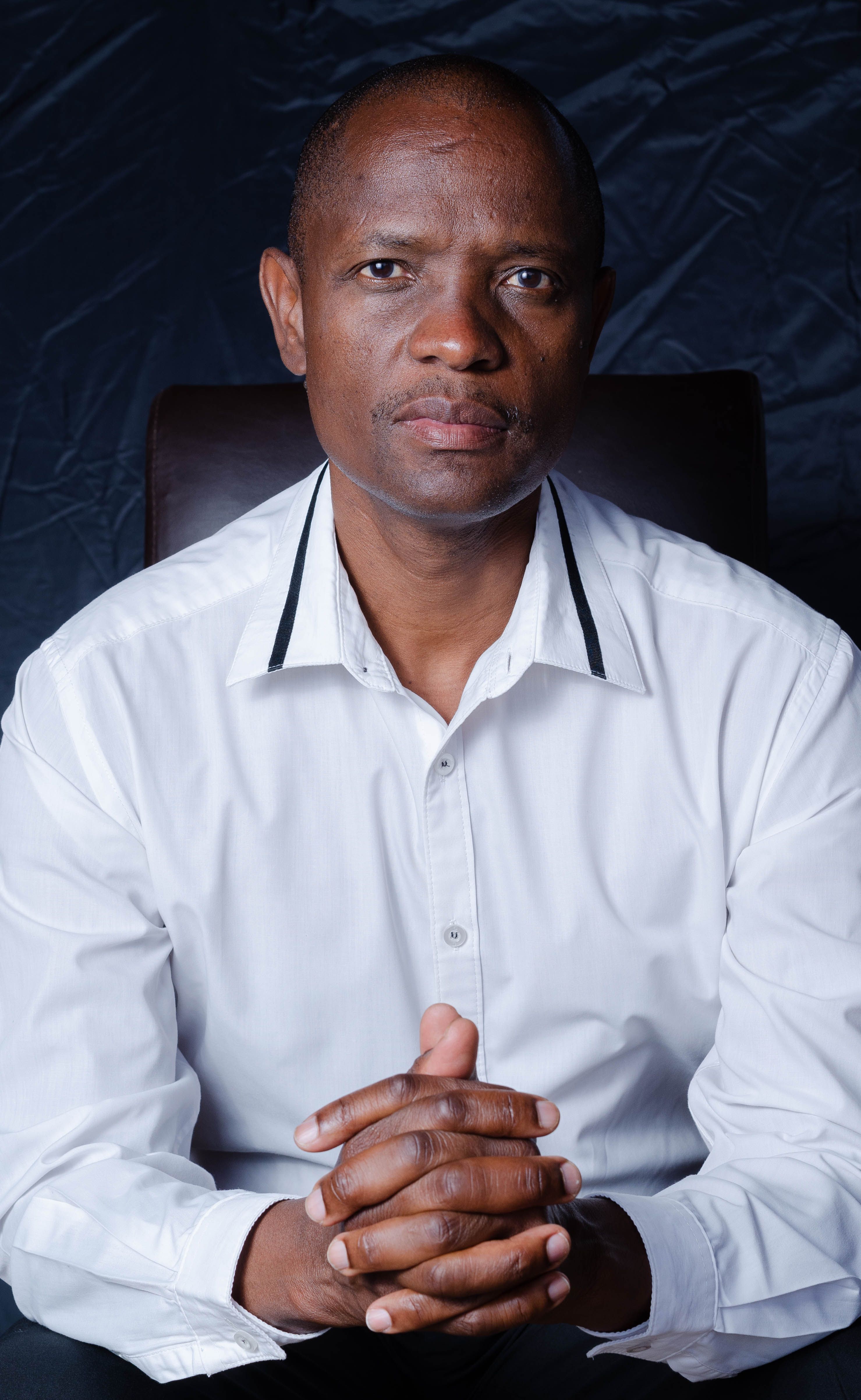 Portrait of a bald African American man in white shirt, indoors, exuding confidence.