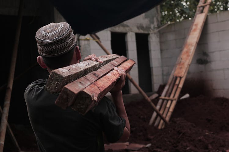 Man Carrying Planks On Building Site