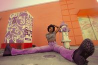 Woman with Curly Hair Wearing Pink Jeans Pants Sitting on Floor in Orange Studio