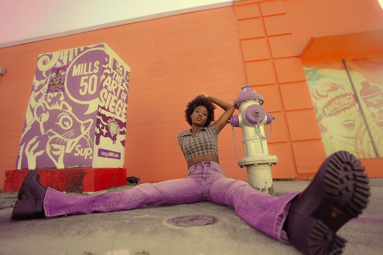 Woman With Curly Hair Wearing Pink Jeans Pants Sitting On Floor In Orange Studio