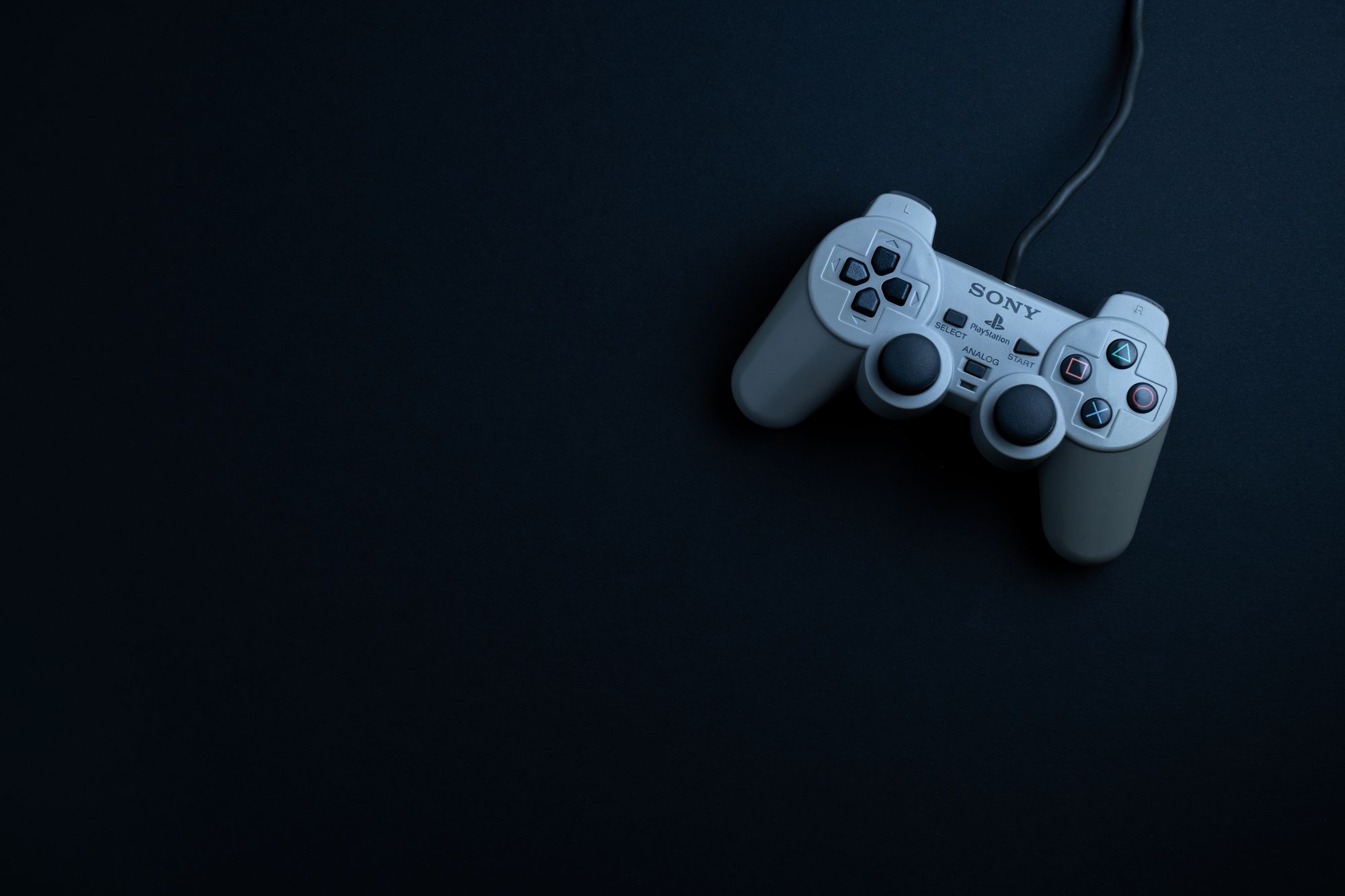 Discos de videojuegos apilados junto a un control de consola sobre una superficie oscura