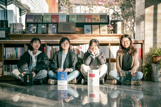 Four young women sitting in a sunny bookstore, enjoying books and friendship.