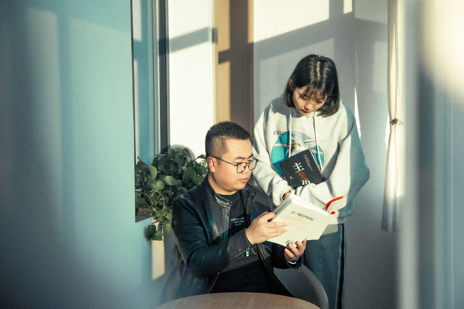 Two adults engaged in reading books in a warmly lit indoor setting.