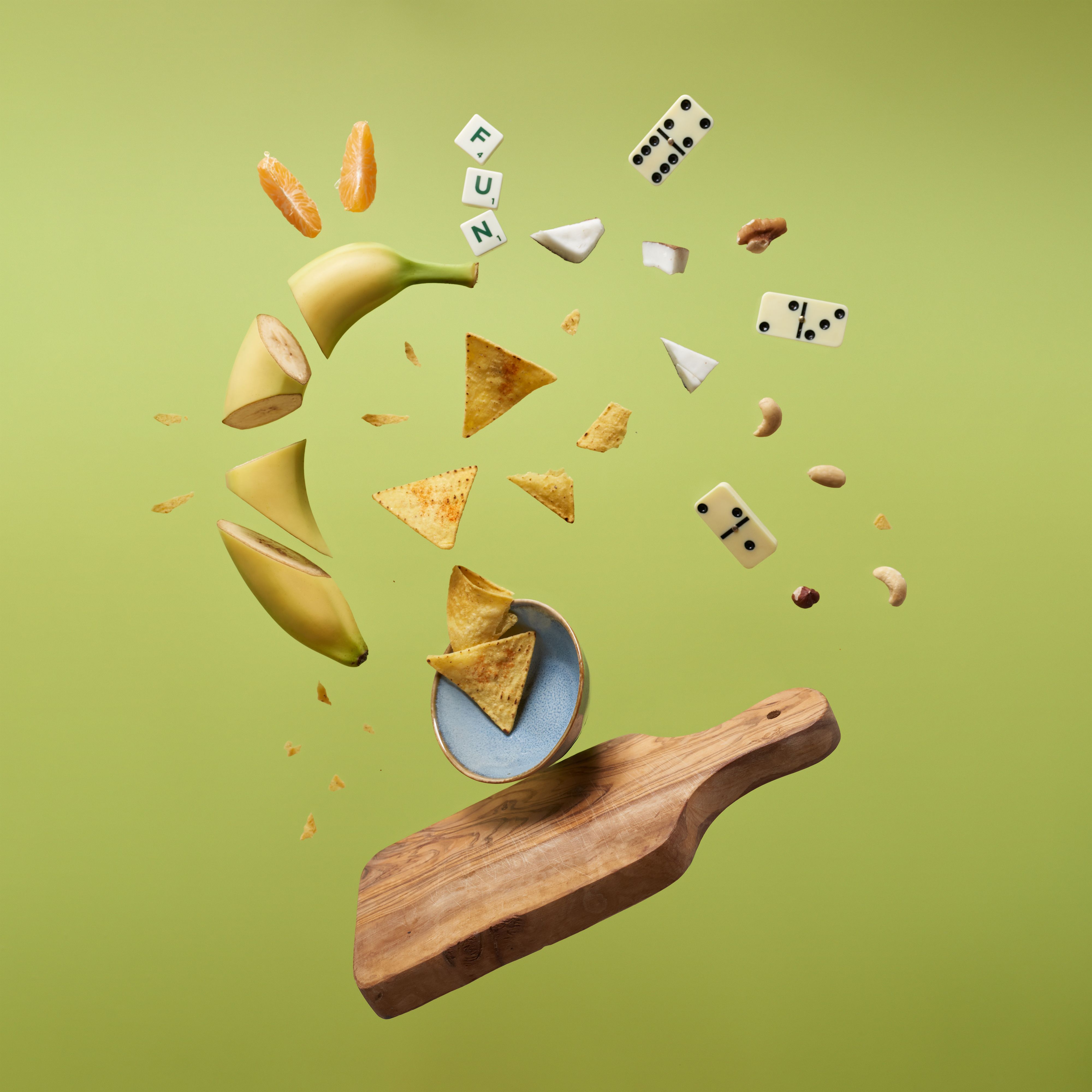 Creative display of floating fruits, dices, and snacks above a chopping board.
