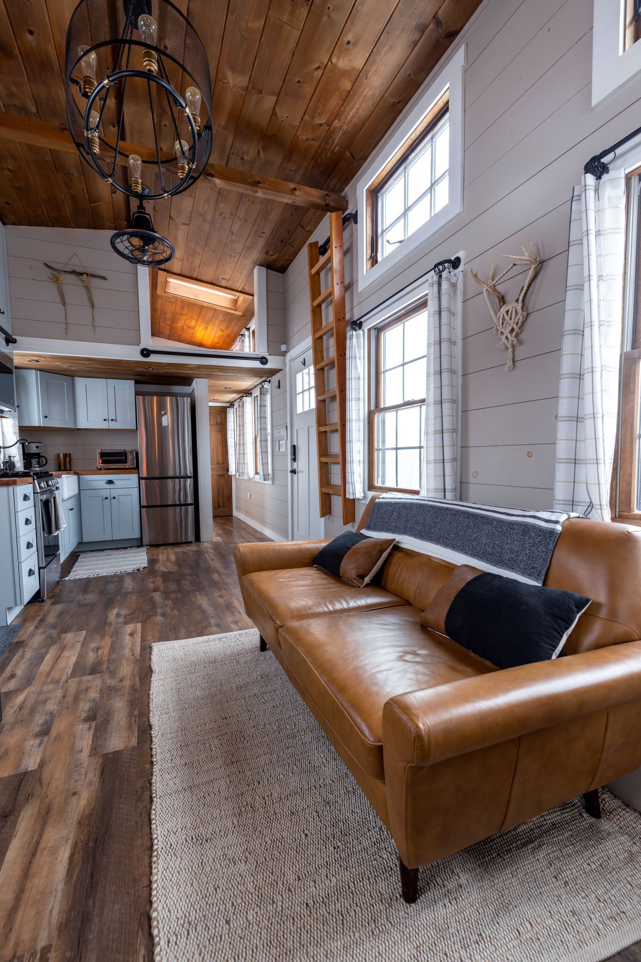 Rustic cabin living room with tan leather sofa, wood plank ceiling, and antler mount