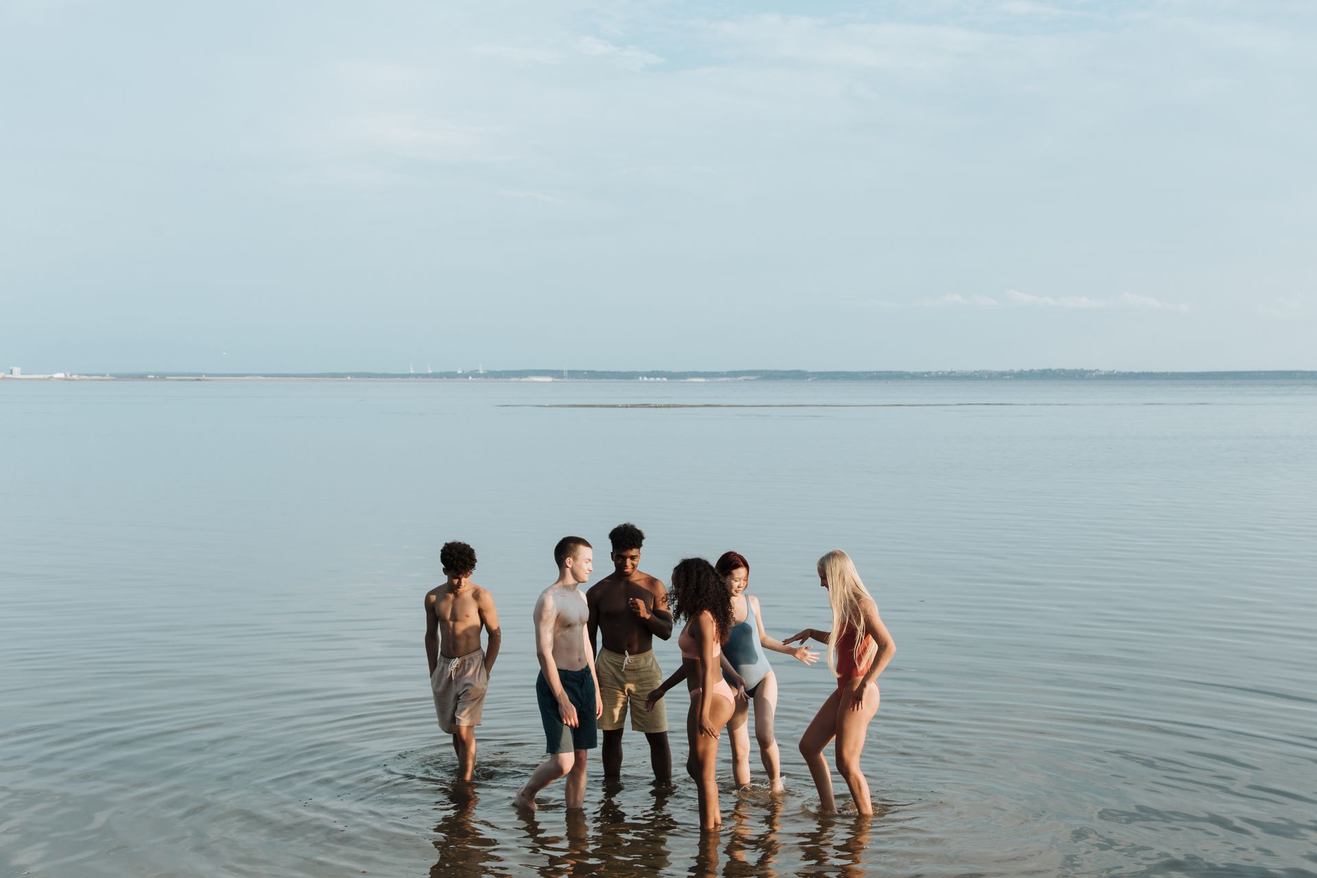 A group of diverse friends enjoying a sunny day at the beach, standing in shallow sea water.