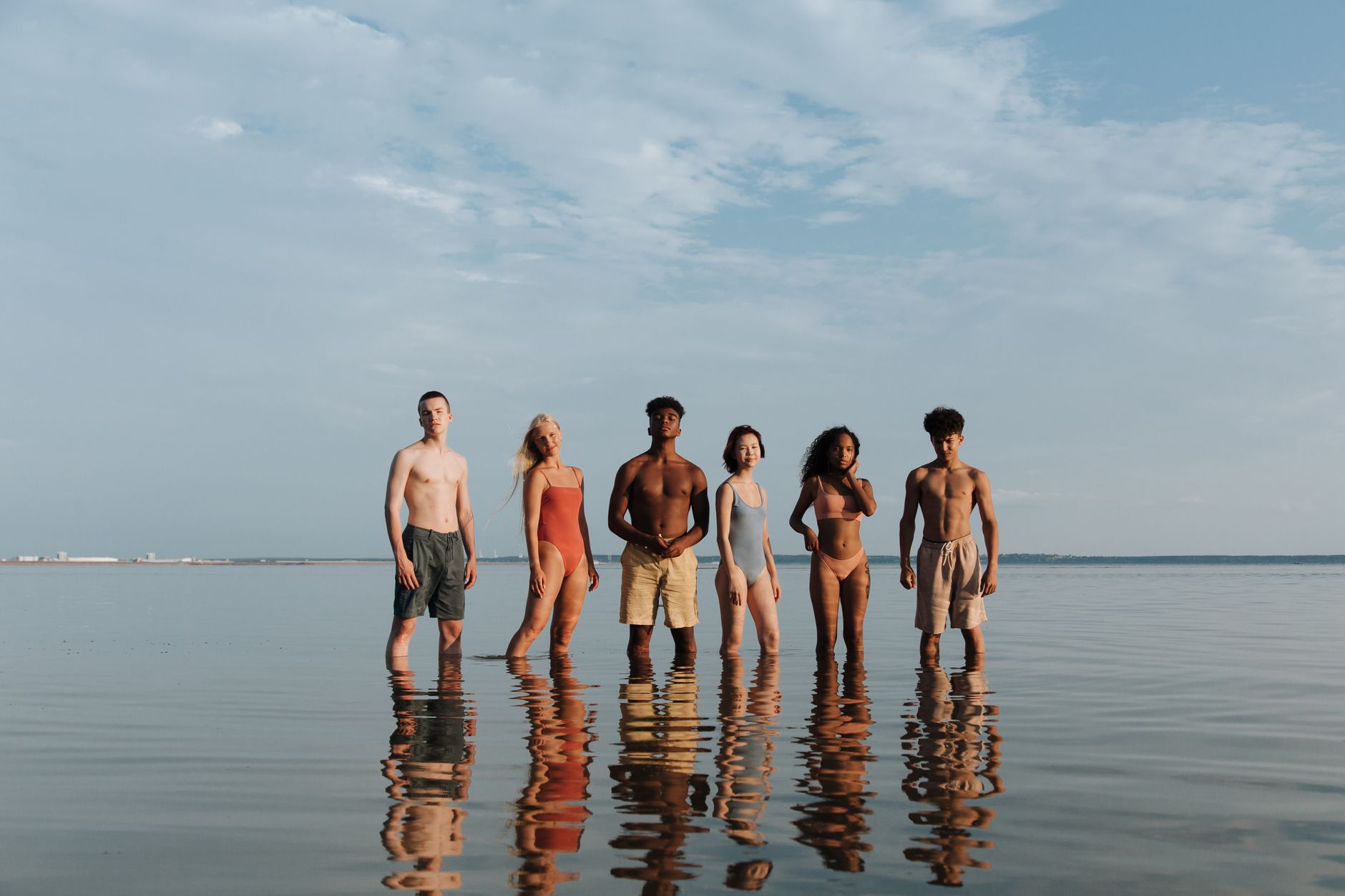 Young adults standing in shallow water at the beach, reflecting summer vibes and diversity.