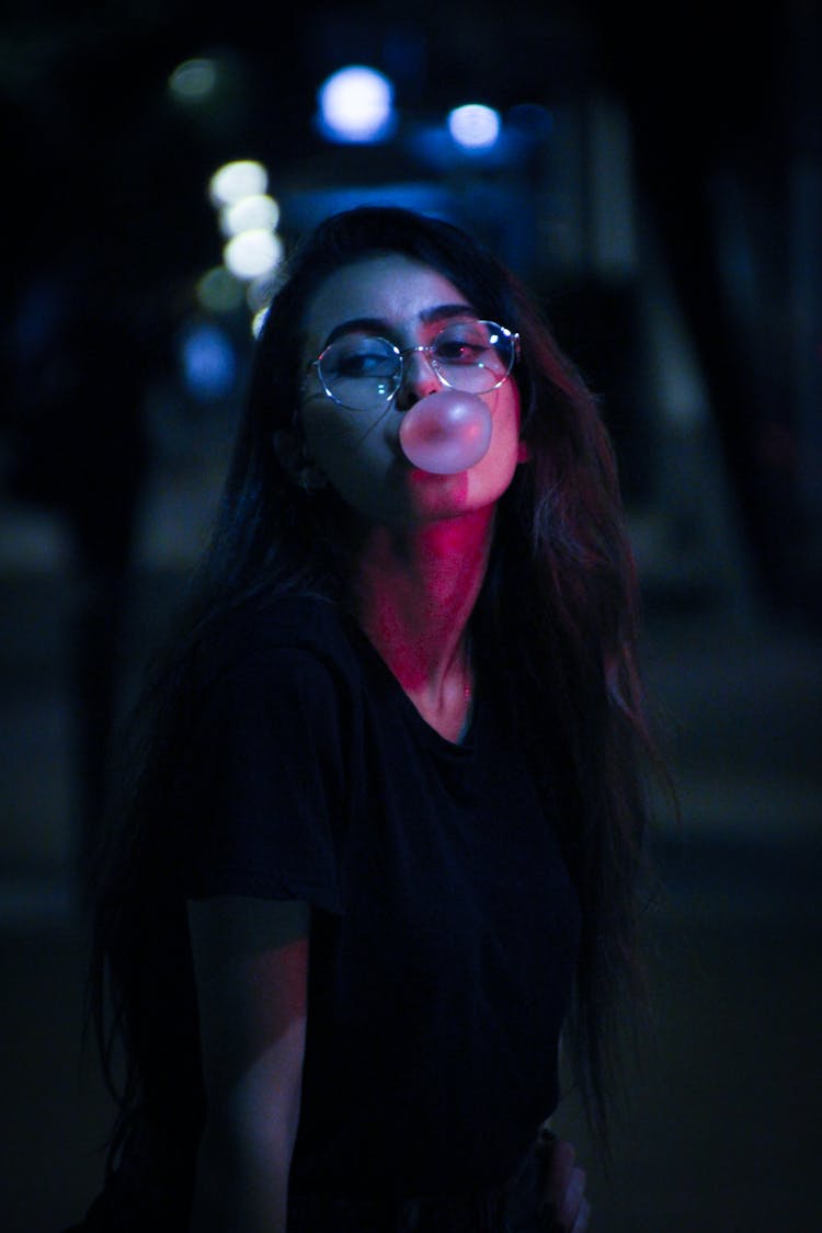 Woman In Black Shirt Wearing Eyeglasses Popping Bubble Gum 