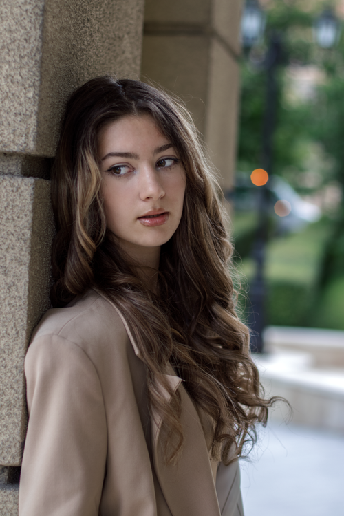 Free Young woman with long hair posing thoughtfully against a wall, captured outdoors. Stock Photo