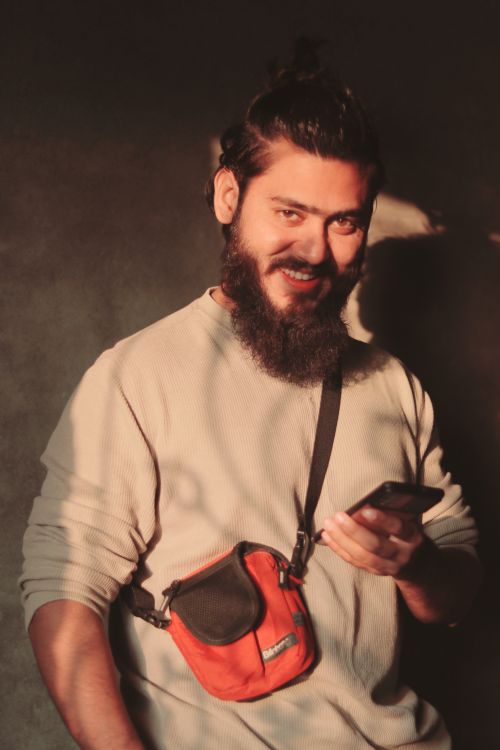 Free Bearded man with a smartphone poses confidently in warm studio lighting. Stock Photo